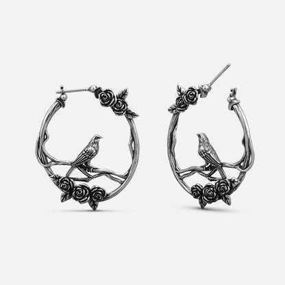 Pair of oxidized silver-tone hoop earrings with rose vine and perched bird design, front view