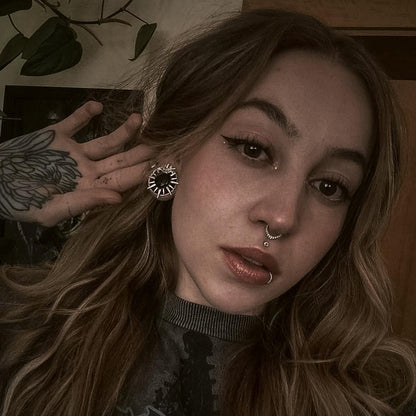 Model with wavy hair wearing a silver-tone sunburst stud earring featuring a dark heart shaped center