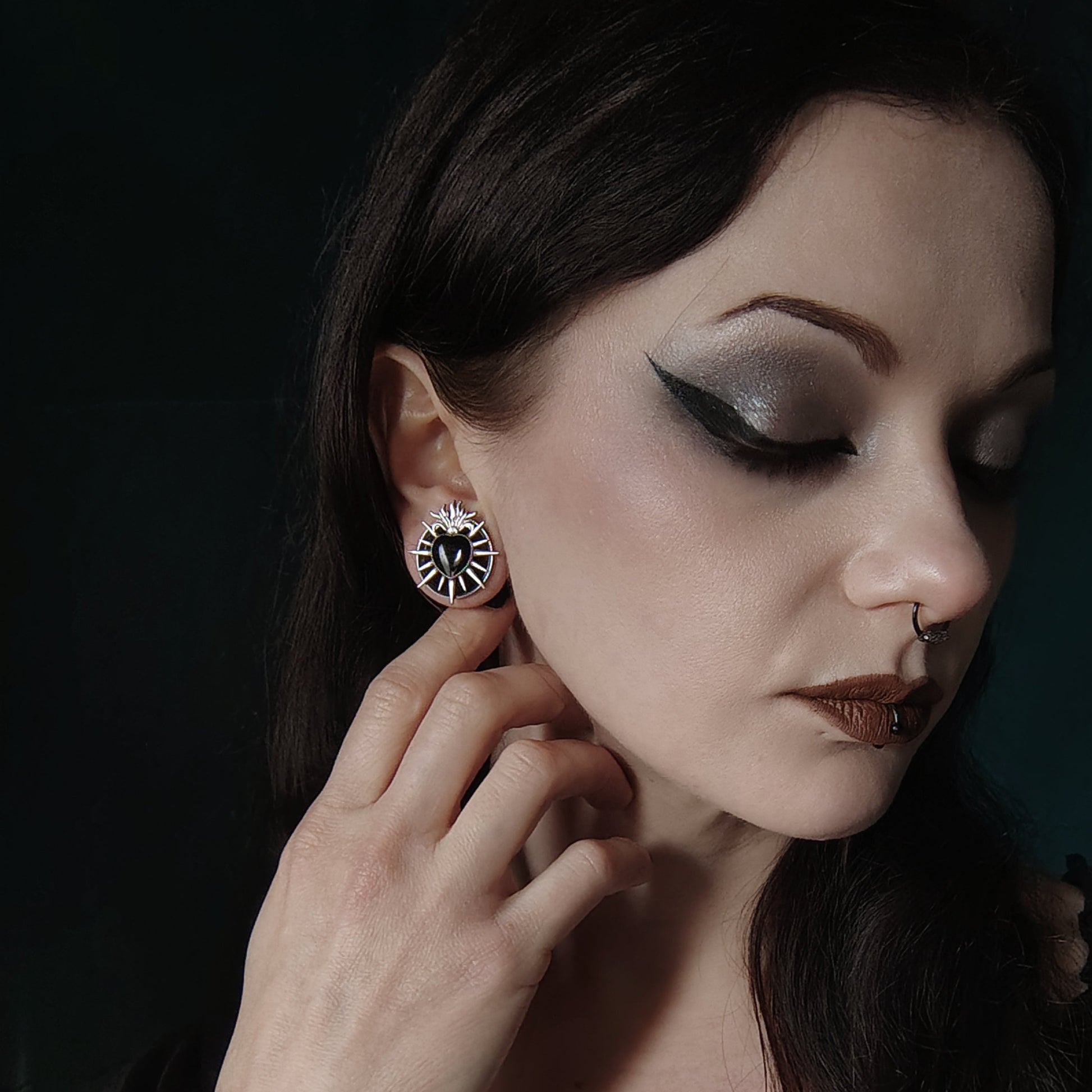 Model wearing a silver-tone heart tunnel stud earring with radiating flame details, close up profile view