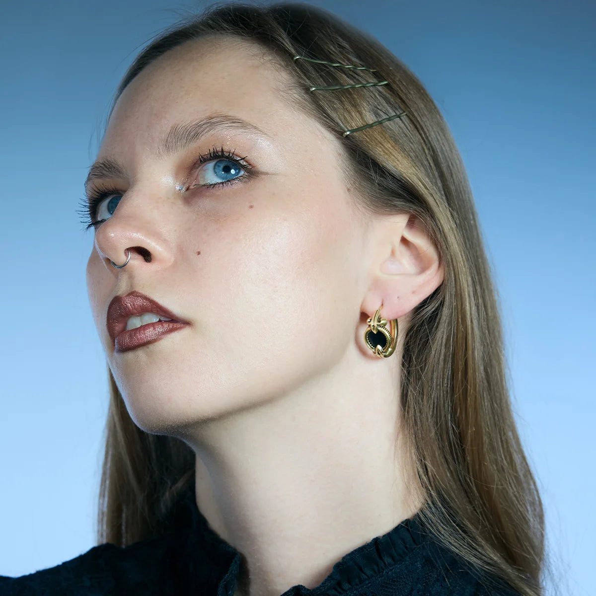 Low-angle side portrait showing a gold-tone Scrying Mirror Hoop Earring with an oval black obsidian inlay.