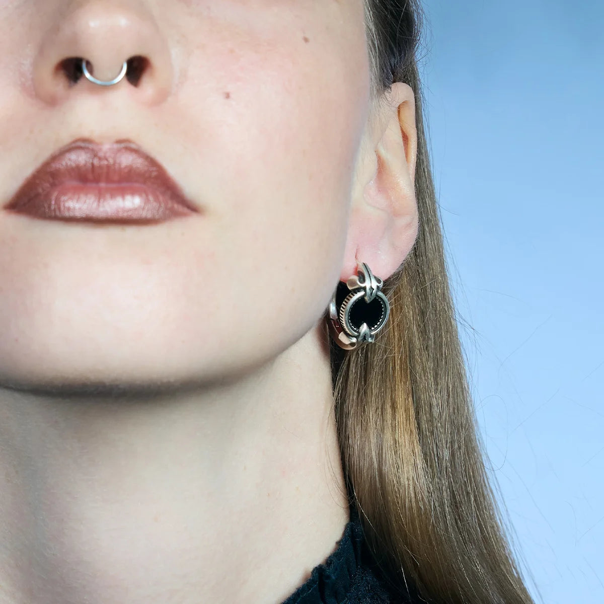 Low-angle close-up of an antiqued silver-tone Scrying Mirror Hoop Earring worn close to the lobe with a black obsidian center.