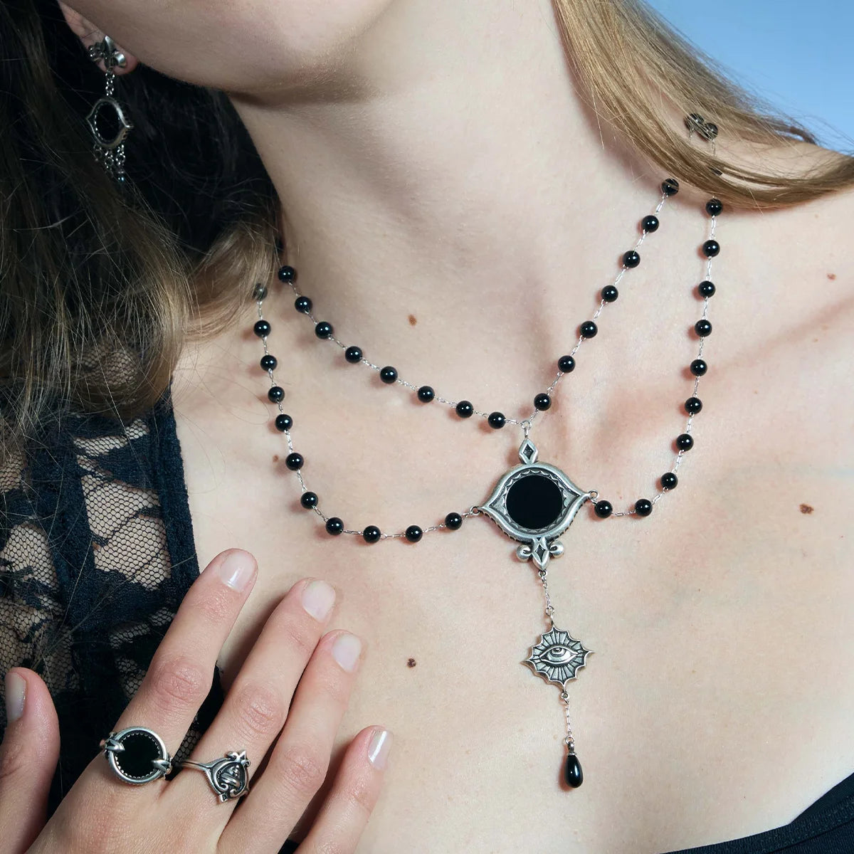 Close-up of an antiqued silver-tone Scrying Mirror Necklace worn at the chest with one hand placed beside the black obsidian centerpiece.