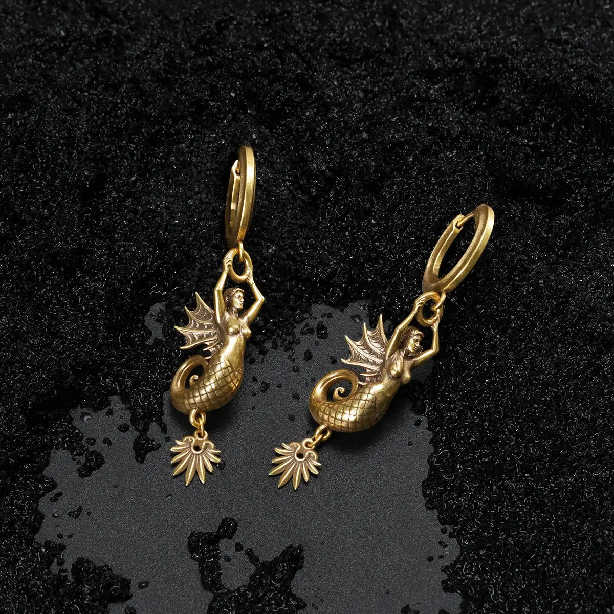 Sea witch aesthetic gold brass siren earrings on textured dark coastal ground