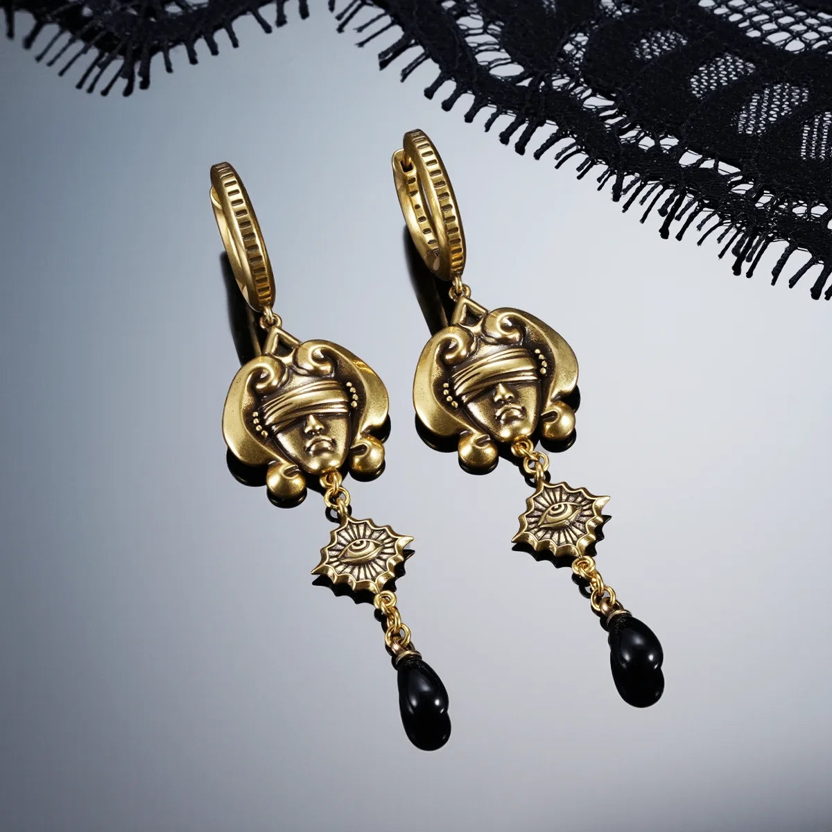 Gold-tone Second Sight Drop Earrings displayed as a pair against black lace on a dark reflective surface.