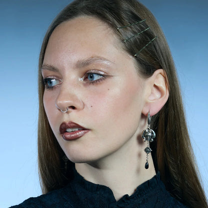 Three-quarter portrait showing antiqued silver-tone Second Sight Drop Earrings with articulated eye medallions and black teardrop accents.
