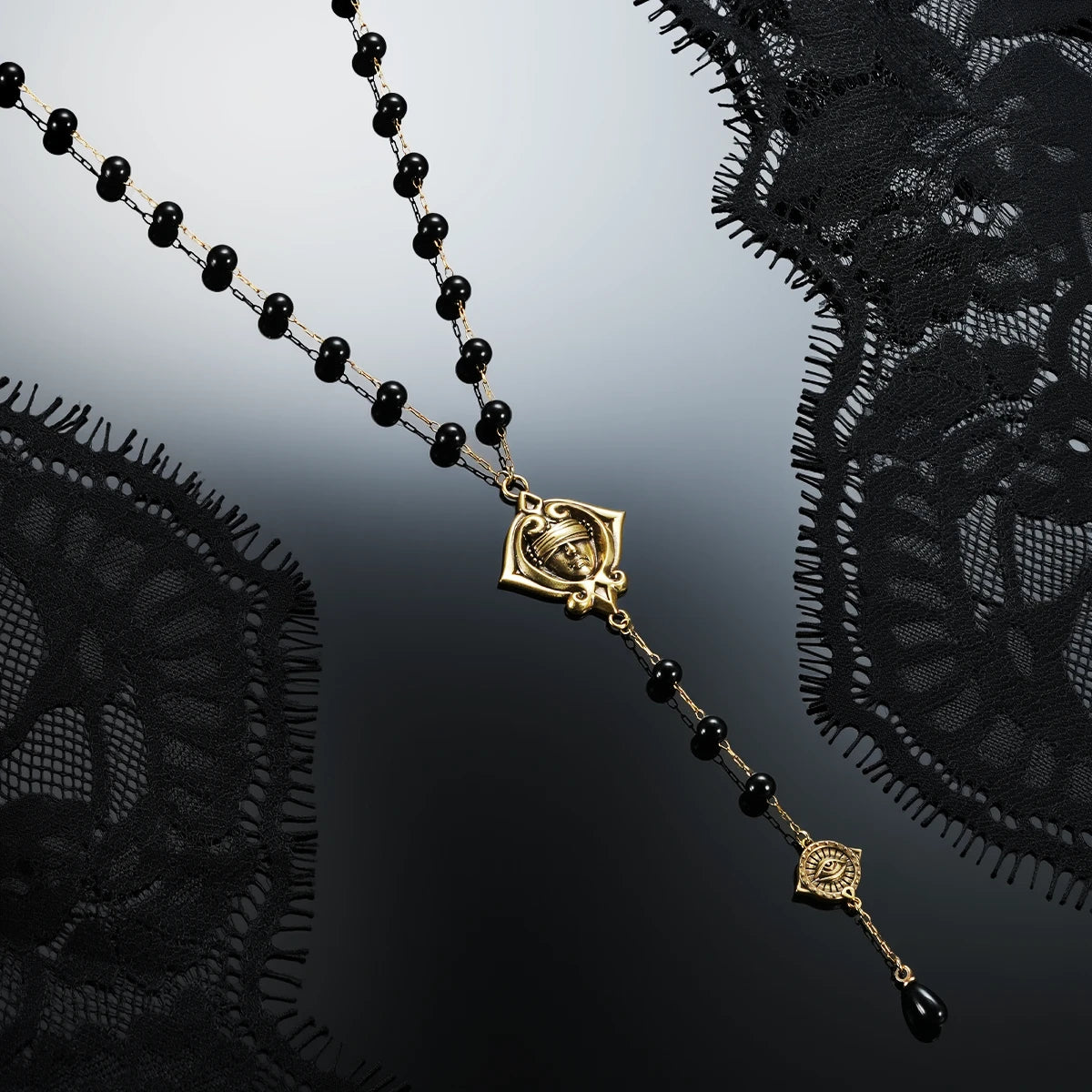 Gold-tone Second Sight Lariat Necklace displayed diagonally against black lace on a dark reflective surface.