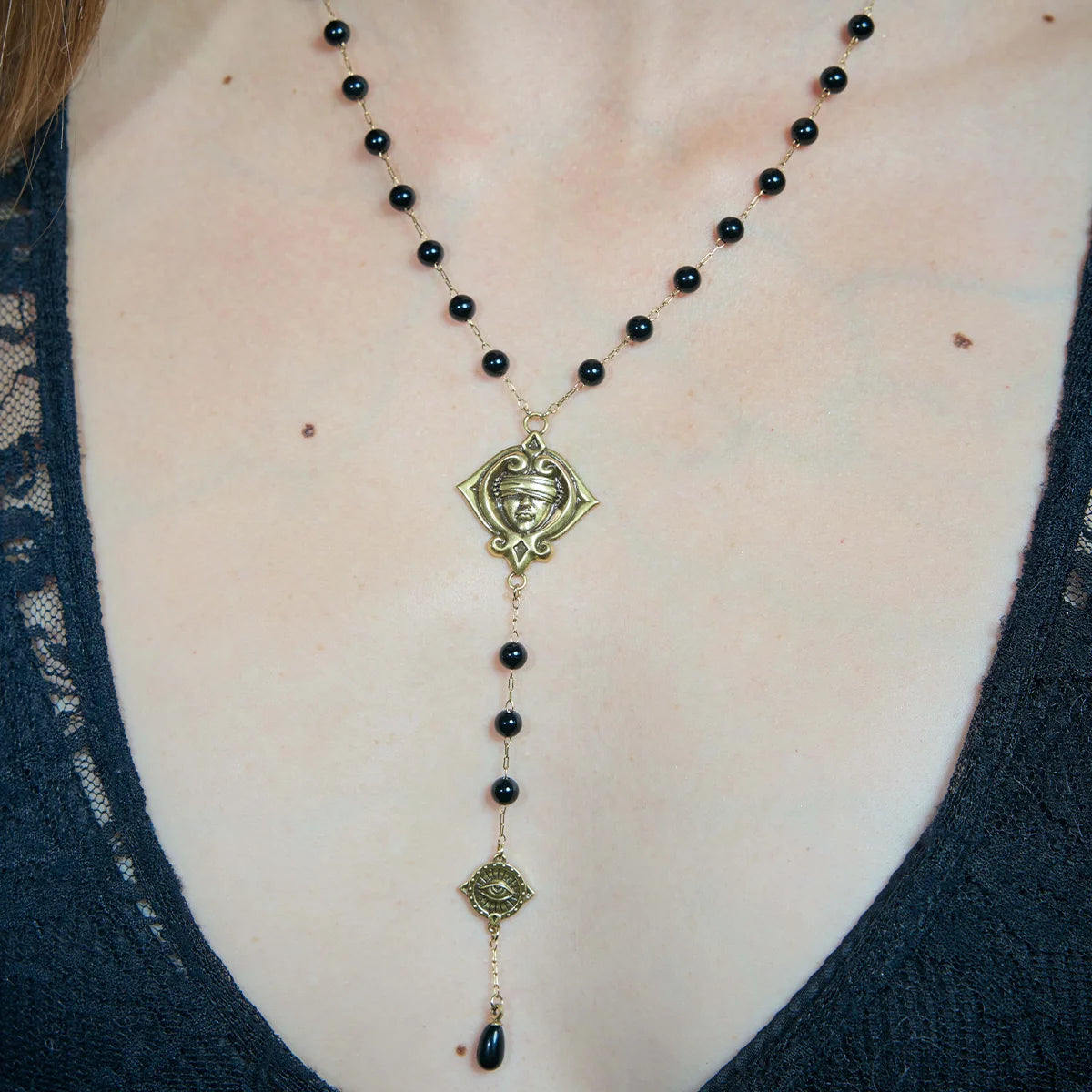 Close-up of a gold-tone Second Sight Lariat Necklace worn at the chest with black beads and a suspended symbolic drop.