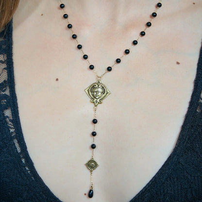 Close-up of a gold-tone Second Sight Lariat Necklace worn at the chest with black beads and a suspended symbolic drop.
