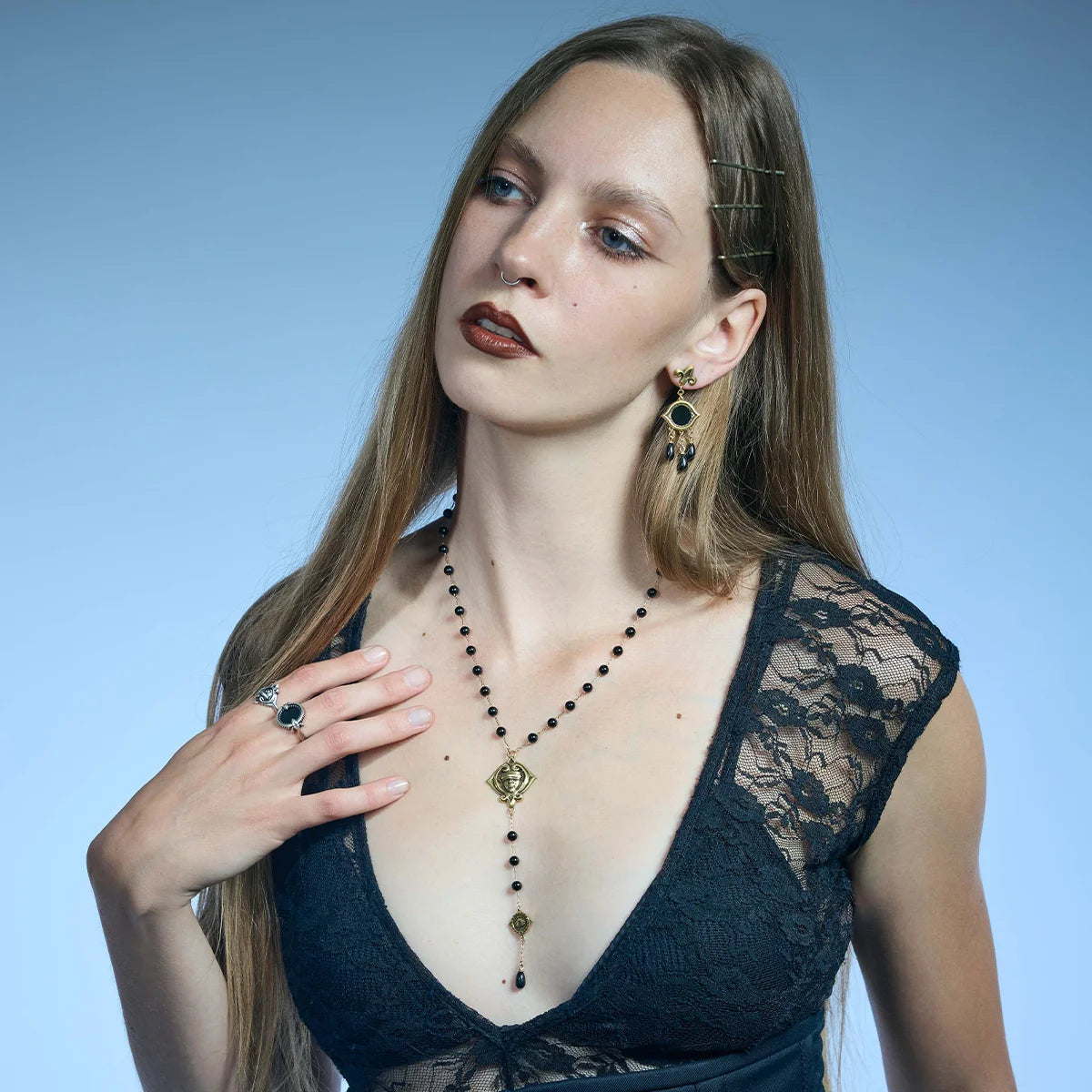 Three-quarter portrait showing a gold-tone Second Sight Lariat Necklace with black beads and an elongated symbolic drop.
