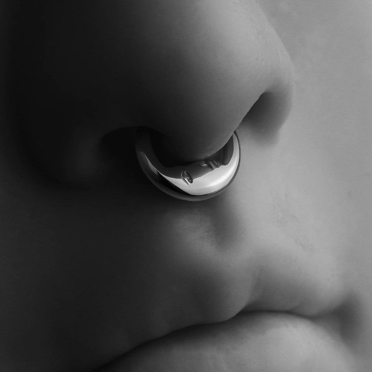 Black and white close-up of a titanium septum ring with a serene face motif worn on the nose