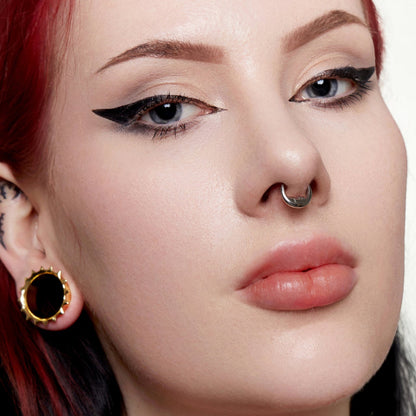 Close-up of a model wearing a titanium septum ring with a serene face design and a gold ear plug