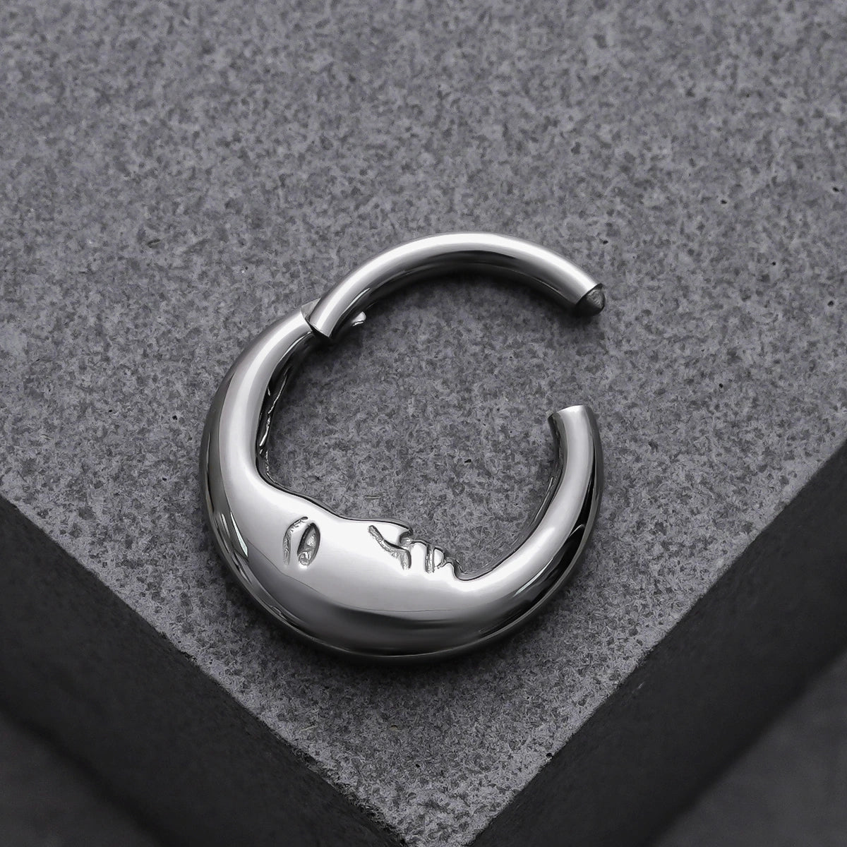 Open silver Serene Face titanium clicker displayed on a gray block
