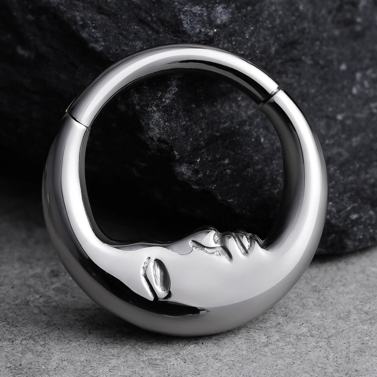 Titanium clicker ring featuring a serene face design displayed against dark stone textures