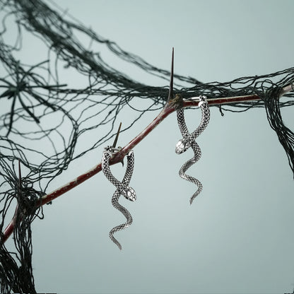 Pair of silver Serpent Grace hoop earrings hanging from a dark branch