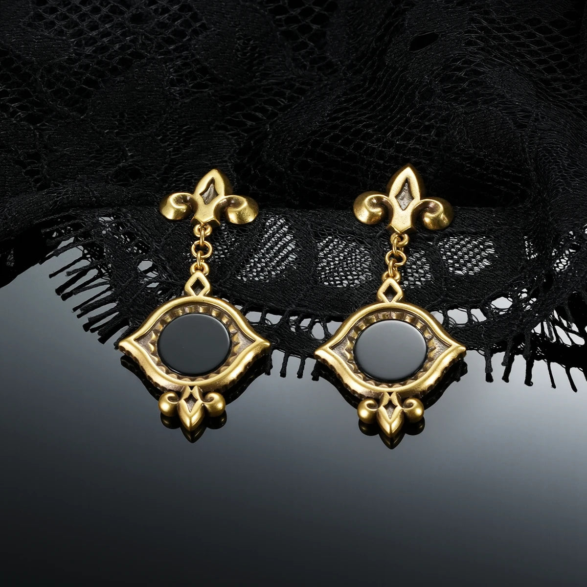 Gold-tone Silent Lens Drop Earrings displayed as a pair against black lace on a dark reflective surface.