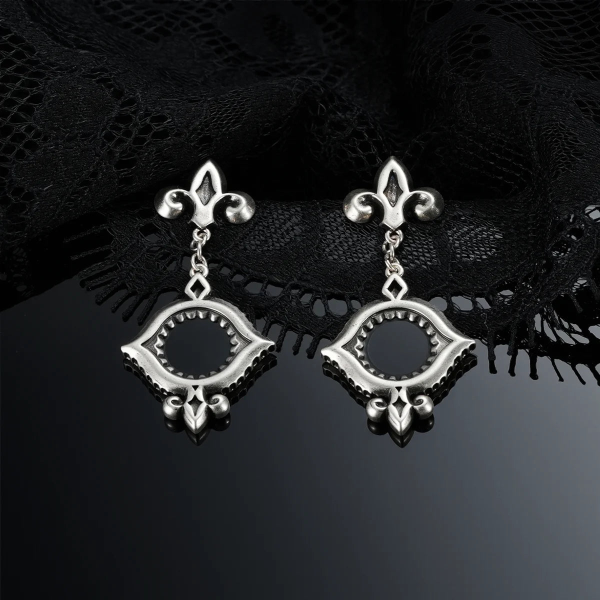 Antiqued silver-tone Silent Lens Drop Earrings displayed as a pair against black lace on a dark reflective surface.