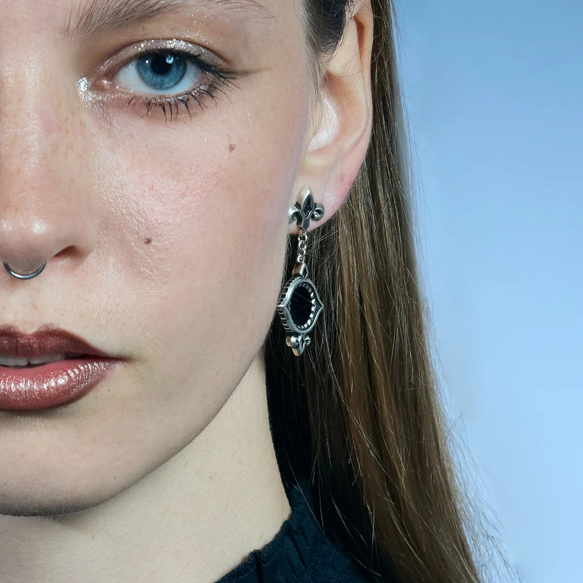 Front close-up of an antiqued silver-tone Silent Lens Drop Earring with a round black obsidian center and fleur-de-lis stud.