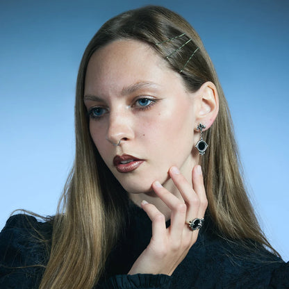 Antiqued silver-tone Silent Lens Drop Earrings worn in a styled portrait, showing the pointed frames and black obsidian inlays.