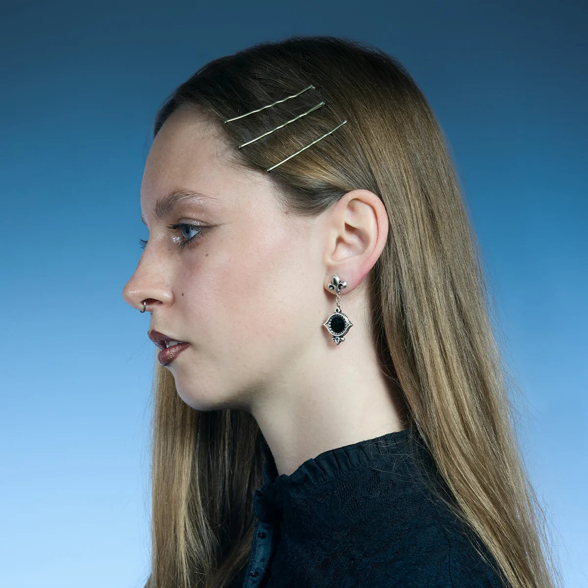 Side portrait showing an antiqued silver-tone Silent Lens Drop Earring suspended below a fleur-de-lis stud.