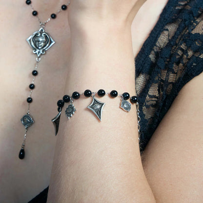 A close-up of a person's wrist and neck wearing a matching gothic jewelry set. The set features black beads, silver spiderweb charms, a spider face pendant, and a spider leg charm.