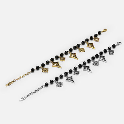 Two beaded bracelets with black round beads and geometric charms, shown in gold and silver metal finishes on a light gray background.