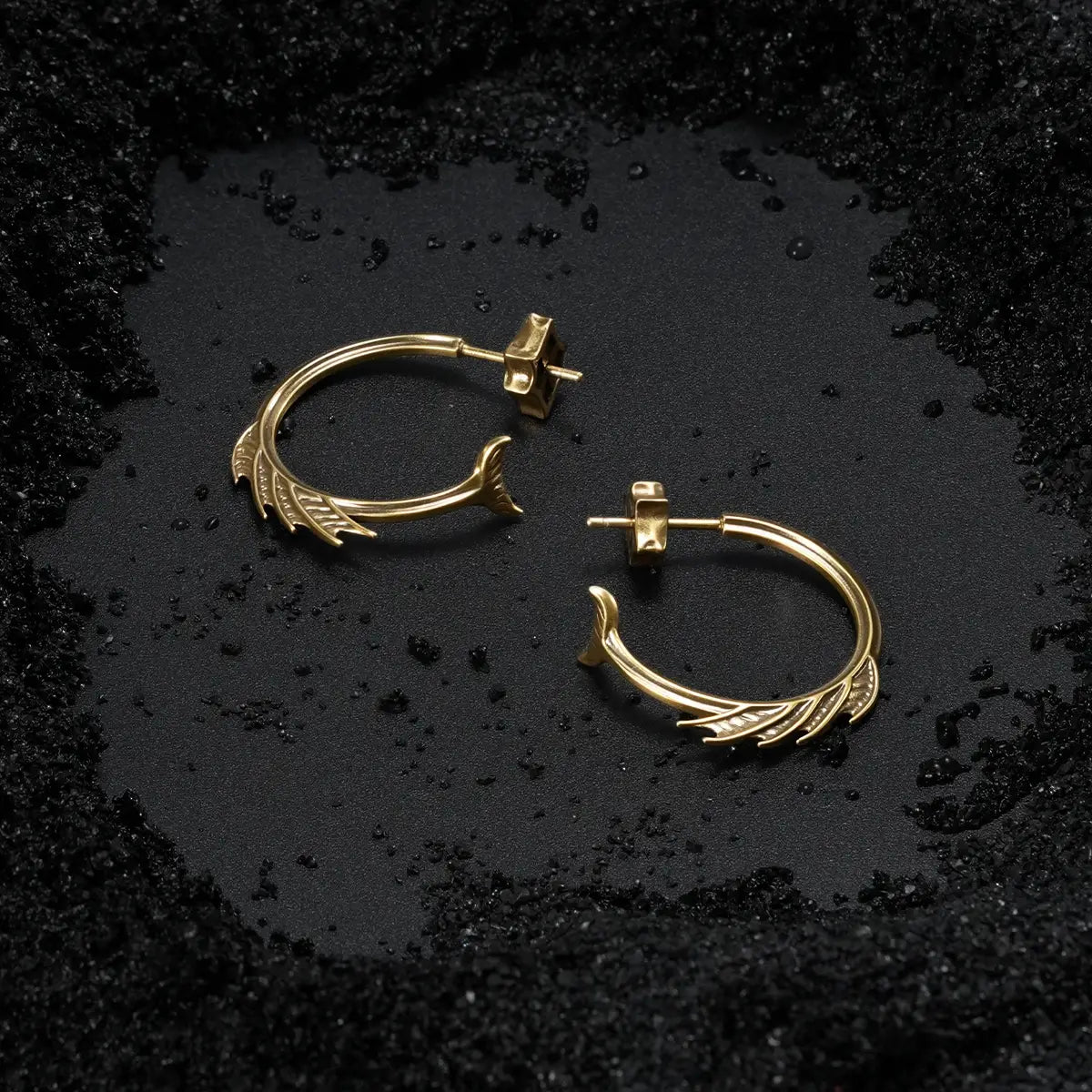 Gold Siren Crest Earrings displayed on black sand, showing the fin-like ridges and sea-worn gothic silhouette.