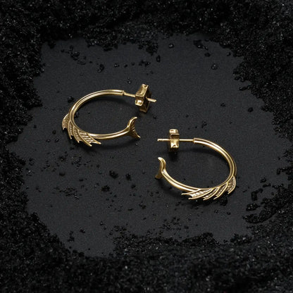 Gold Siren Crest Earrings displayed on black sand, showing the fin-like ridges and sea-worn gothic silhouette.