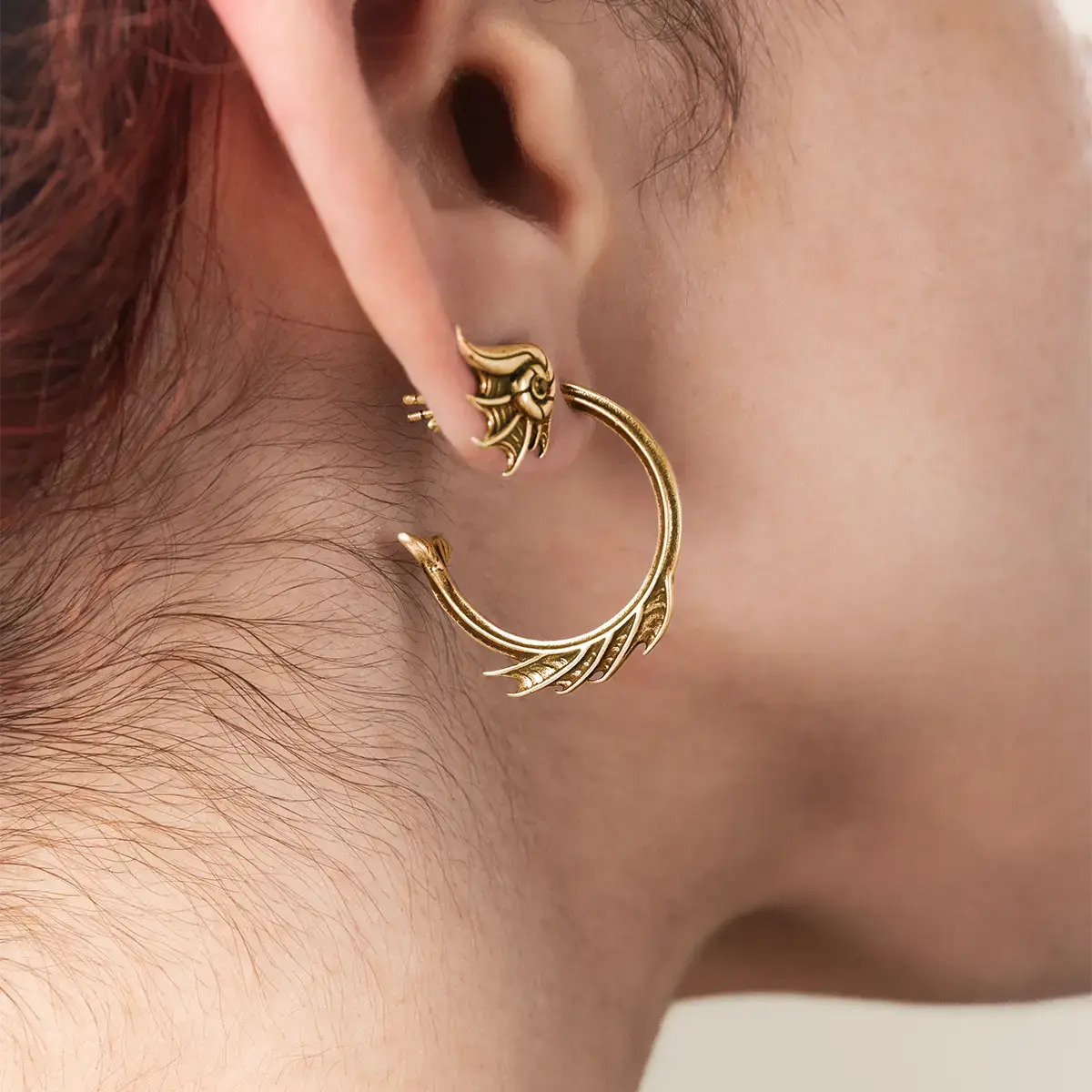 Model wearing the gold Siren Crest Earrings, highlighting the sharp fin-like ridges and curved half-hoop shape.