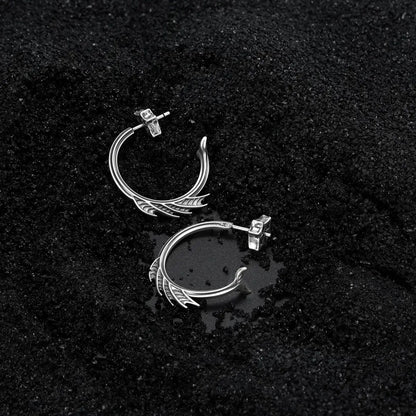 Silver Siren Crest Earrings displayed on black sand, highlighting the sculptural half-hoop shape and ocean relic mood.