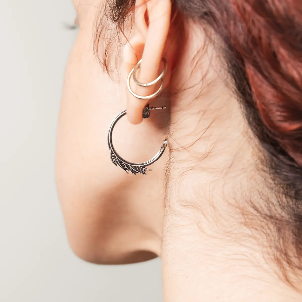 Model wearing the silver Siren Crest Earrings, showing the curved half-hoop silhouette and fin-like ridge details on the ear.