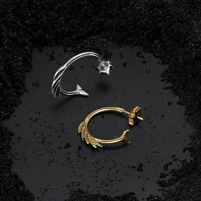 Silver and gold Siren Crest Earrings displayed on black sand, featuring curved half-hoop shapes and sharp fin-like ridge details.