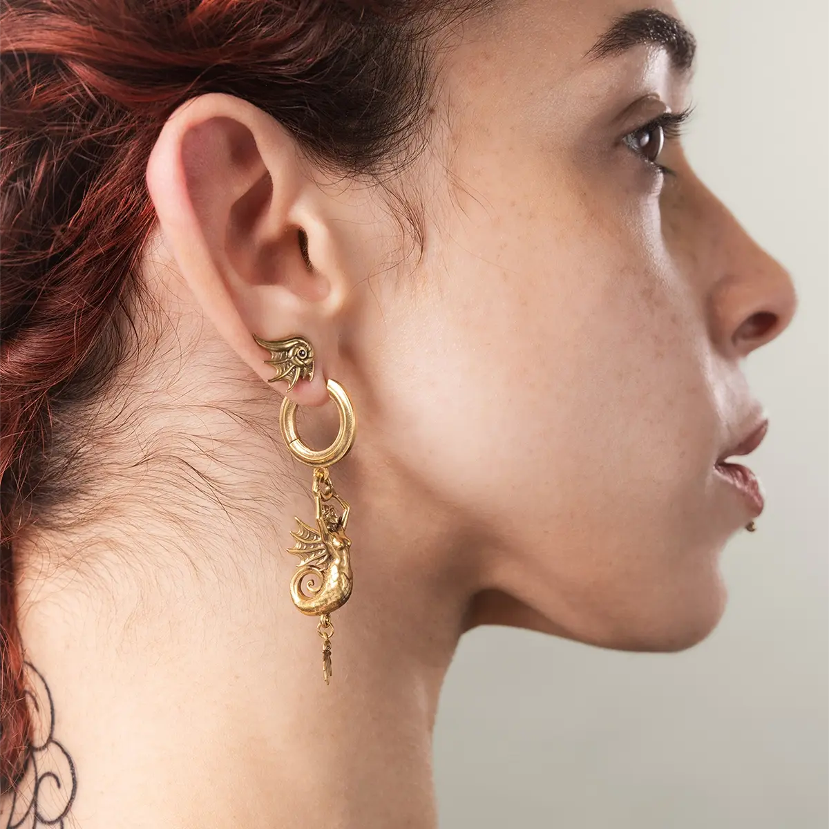 Model wearing the gold Siren's Dirge Earrings, showing the sculpted siren drop silhouette and mythic gothic styling.