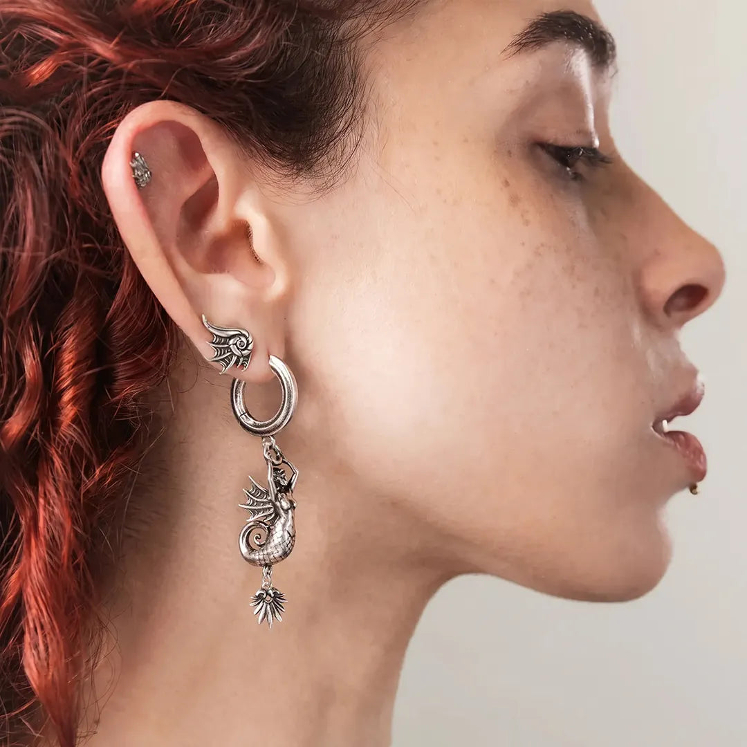 Model wearing Siren's Dirge Earrings featuring sculpted siren figures with scaled tails, sharp fin details, and dangling charms, creating a mythical gothic drop silhouette inspired by dark ocean legends and dangerous beauty.