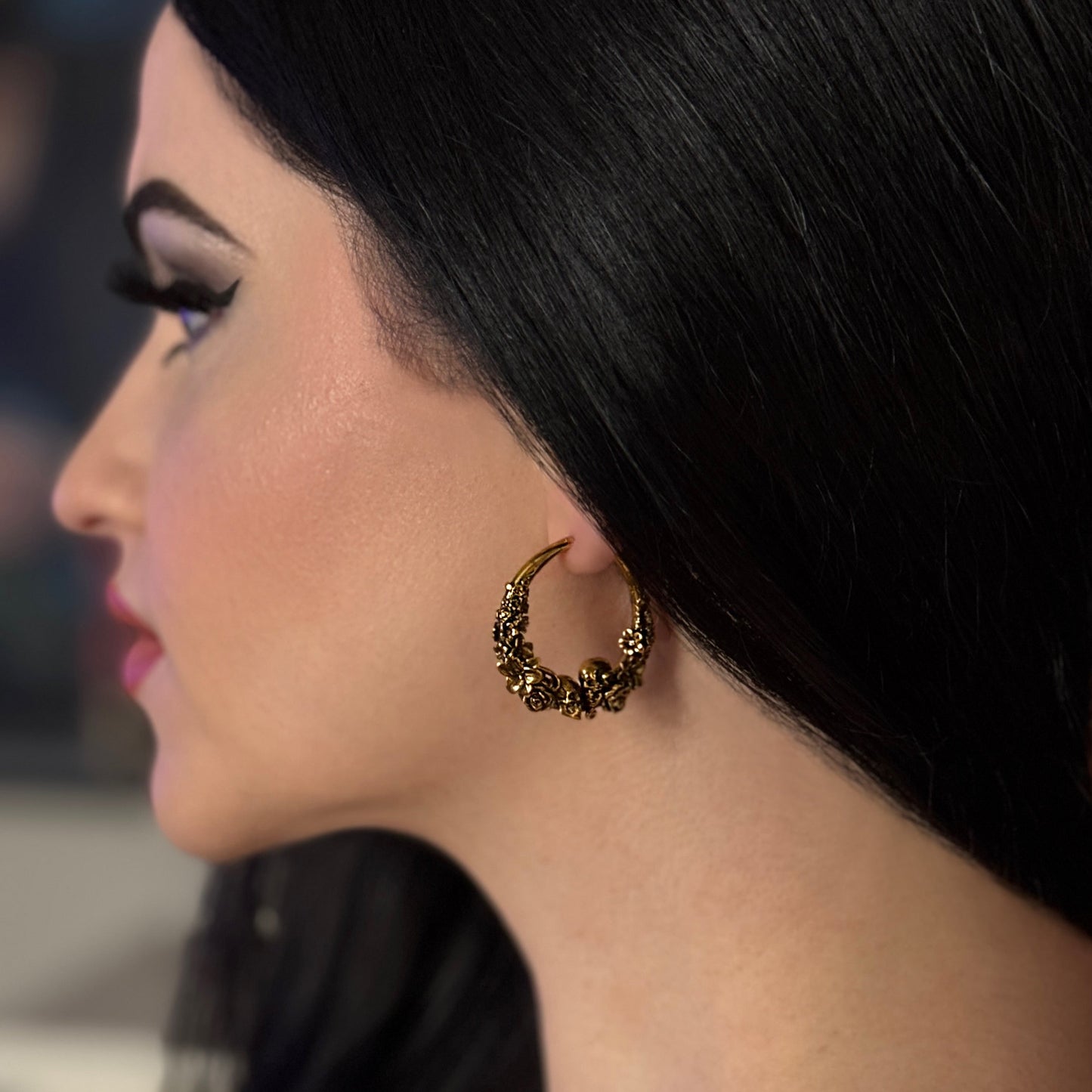 Model wearing an antique gold-tone skull and rose hoop earring, close-up side profile view