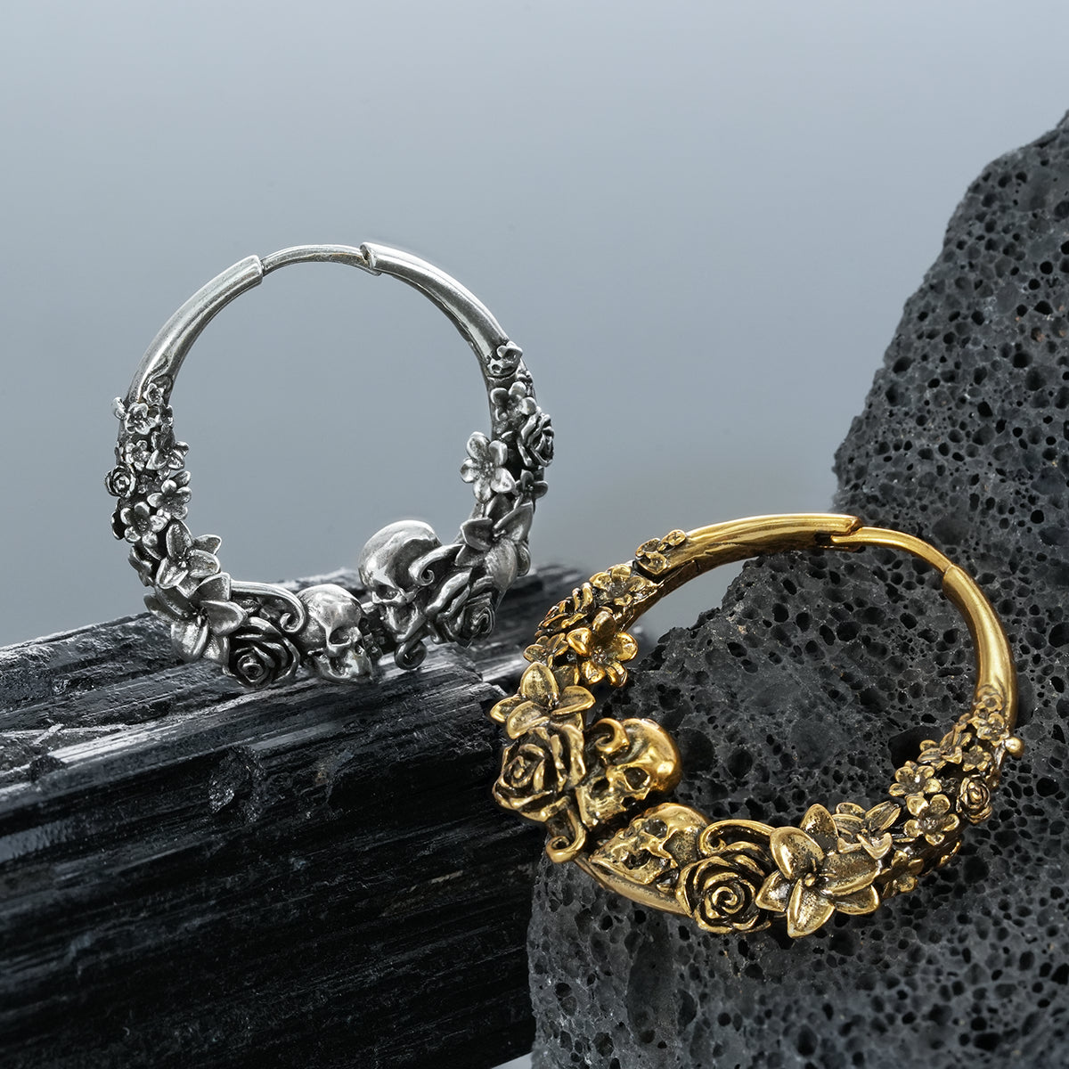 Gold and silver Skull Blossom hoop earrings displayed on dark stones