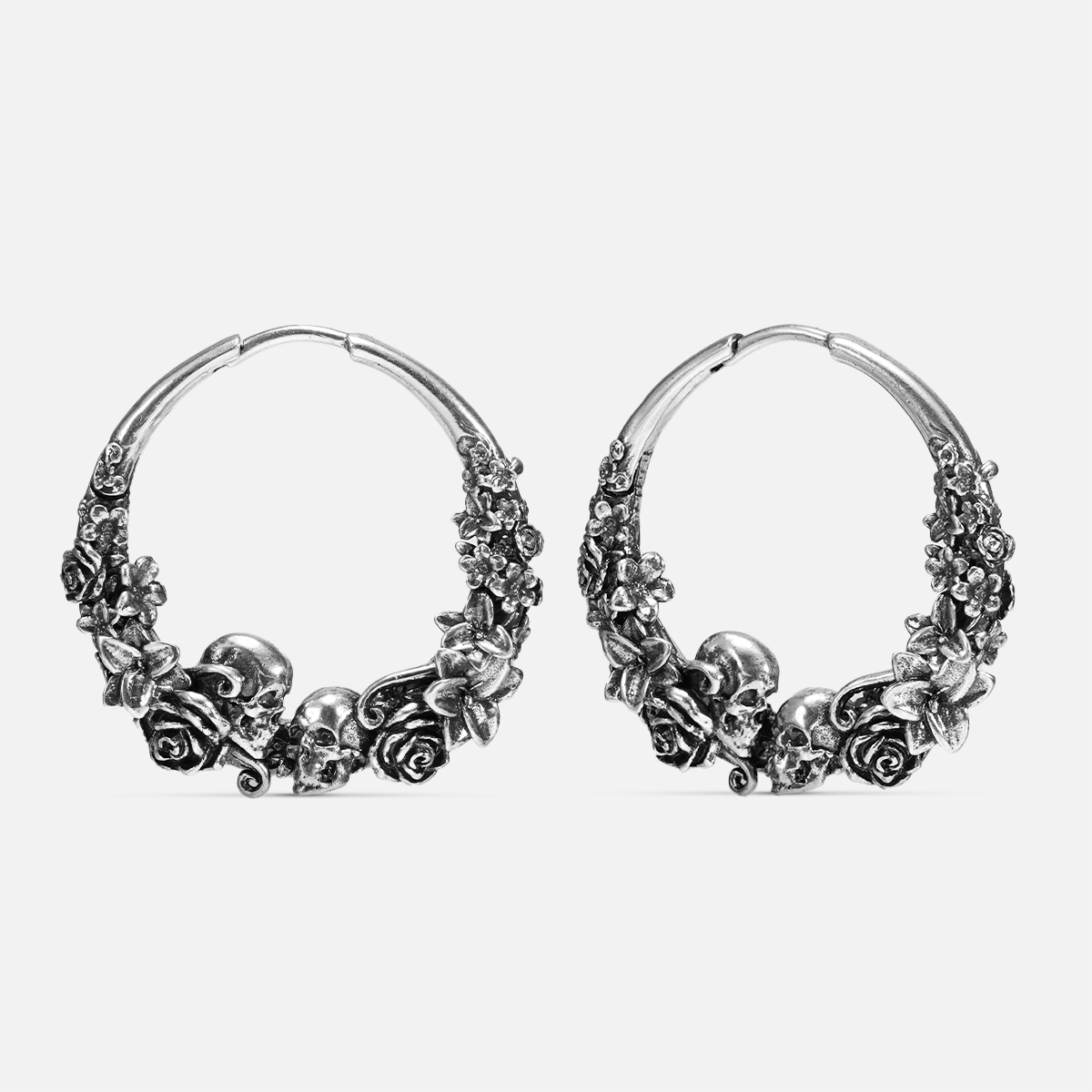 Pair of oxidized silver-tone hoop earrings featuring skull and rose blossom design, front view on white background