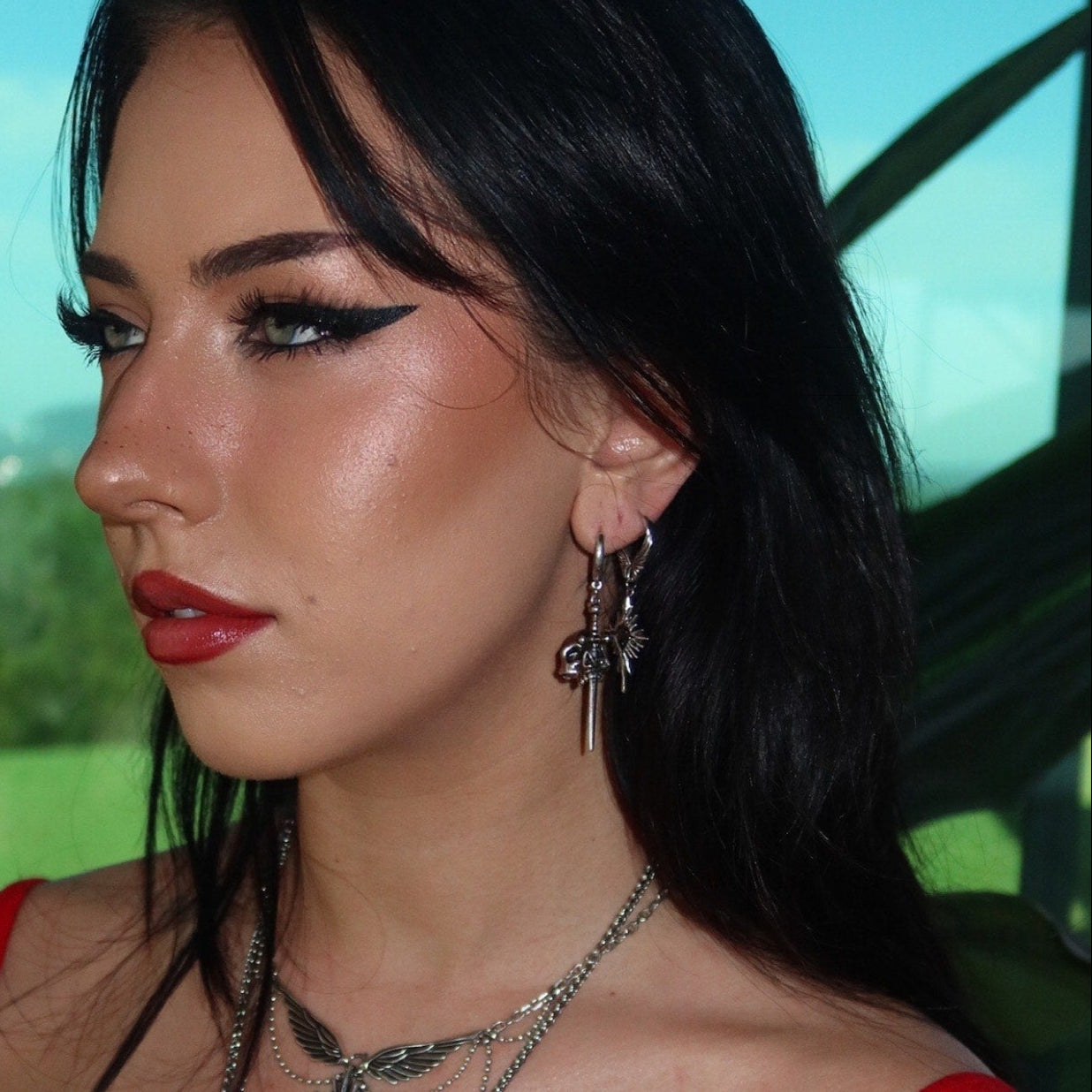 Model wearing a silver Skull Dagger hoop earring with layered necklaces