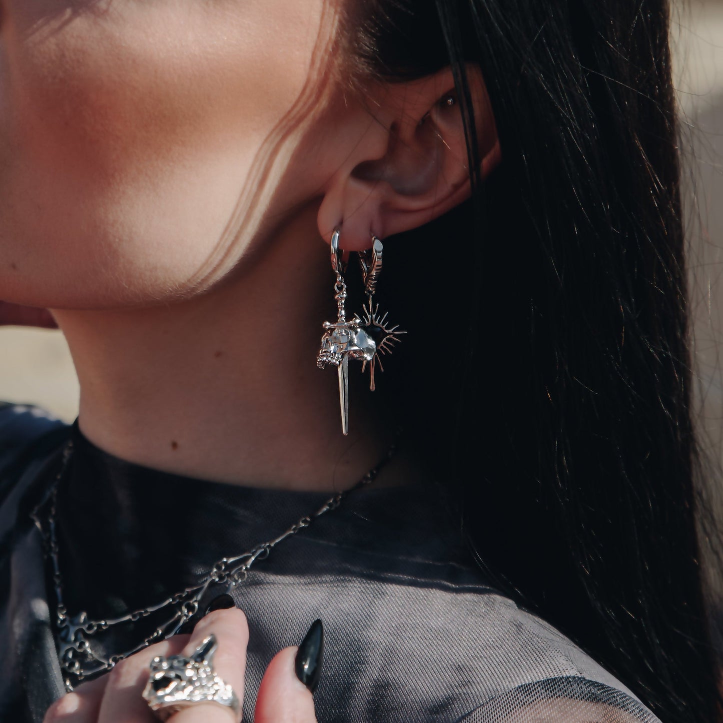 Close-up of silver Skull Dagger hoop earring worn on the earlobe