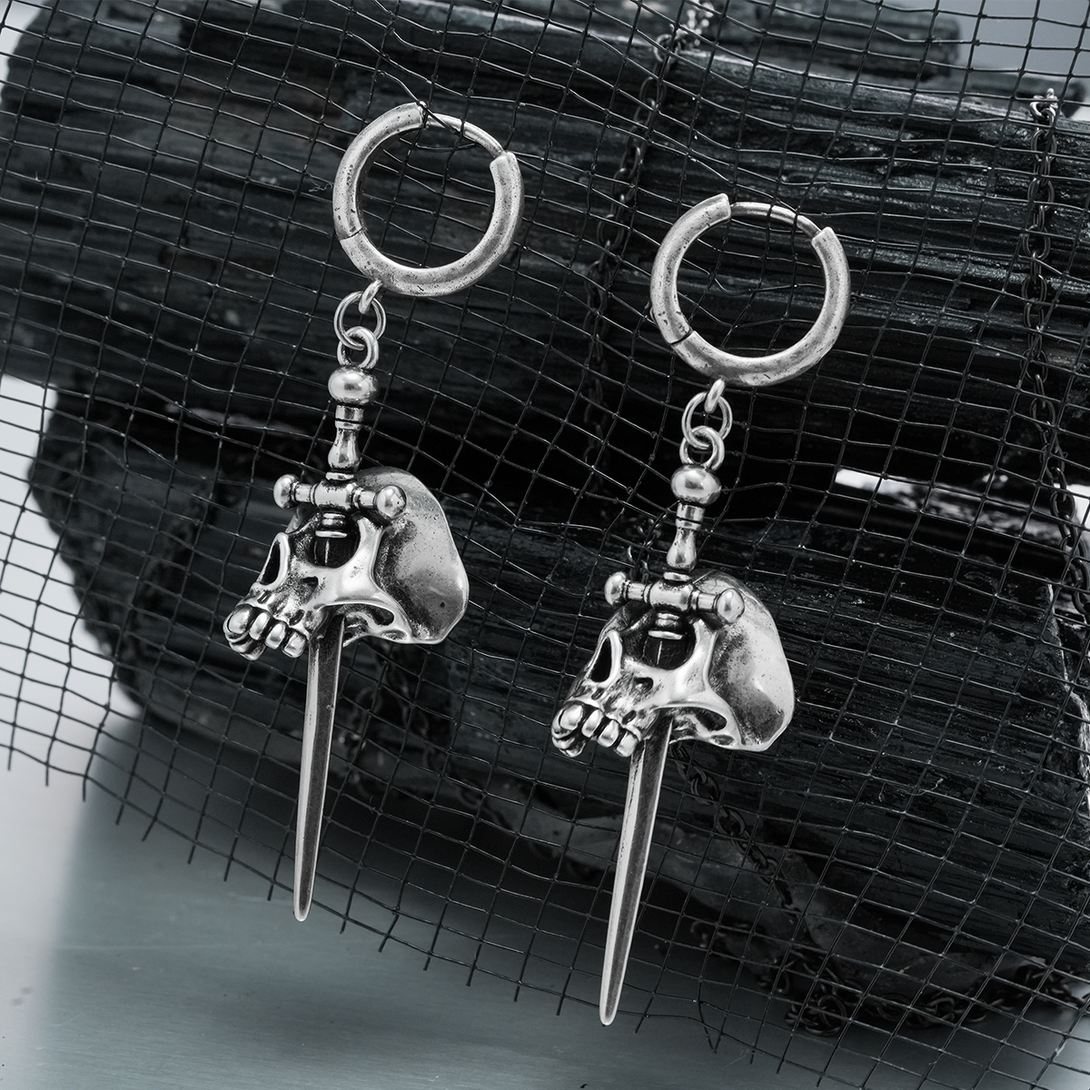 Pair of silver Skull Dagger hoop earrings displayed against black mesh