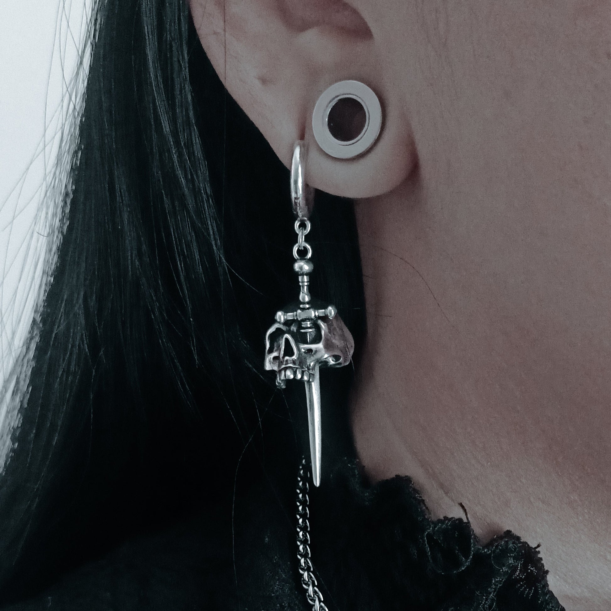 Close-up of a model wearing a silver-tone skull dagger drop earring with hoop and chain