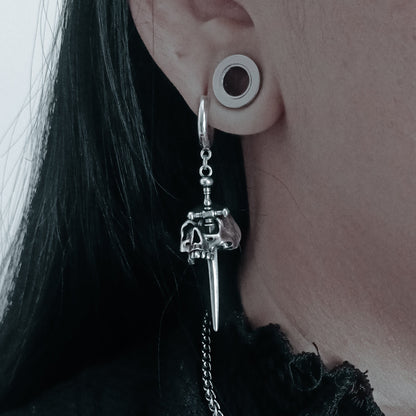 Close-up of a model wearing a silver-tone skull dagger drop earring with hoop and chain