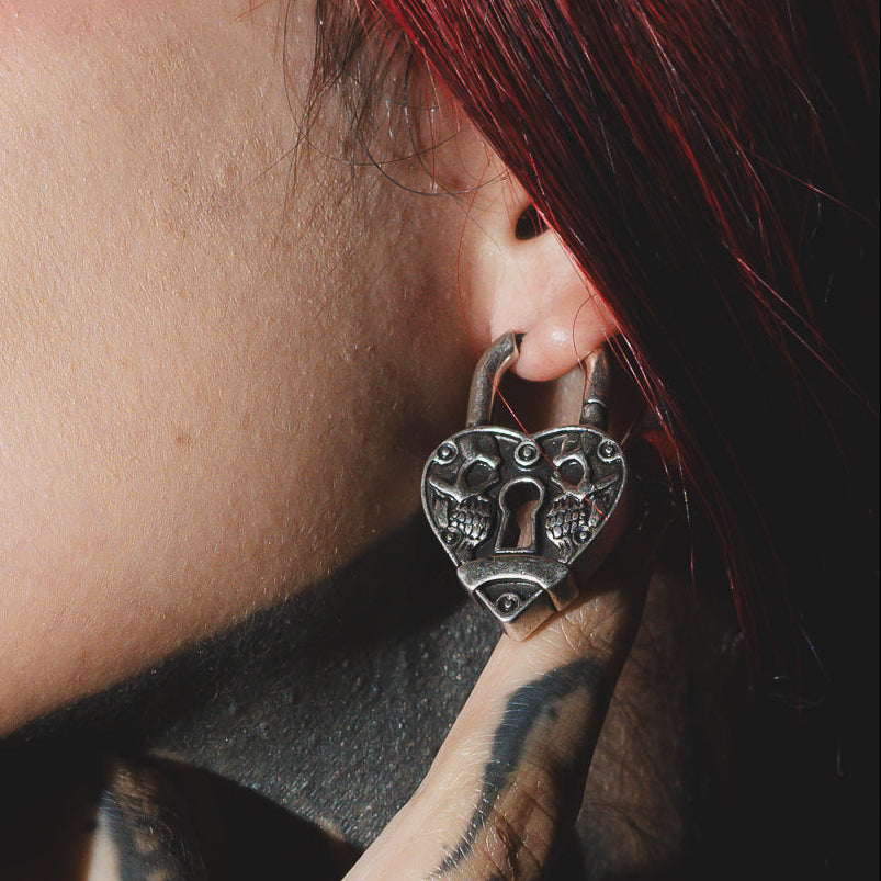 Close-up of a silver-tone skull heartlock hoop earring worn on a model's ear