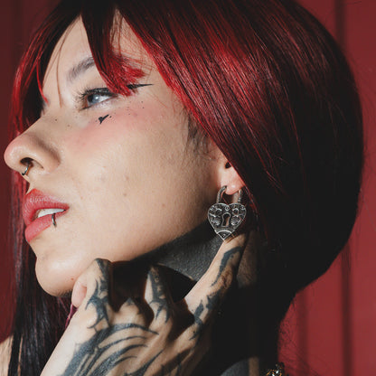 Model wearing a silver-tone skull heartlock hoop earring, side profile with red hair