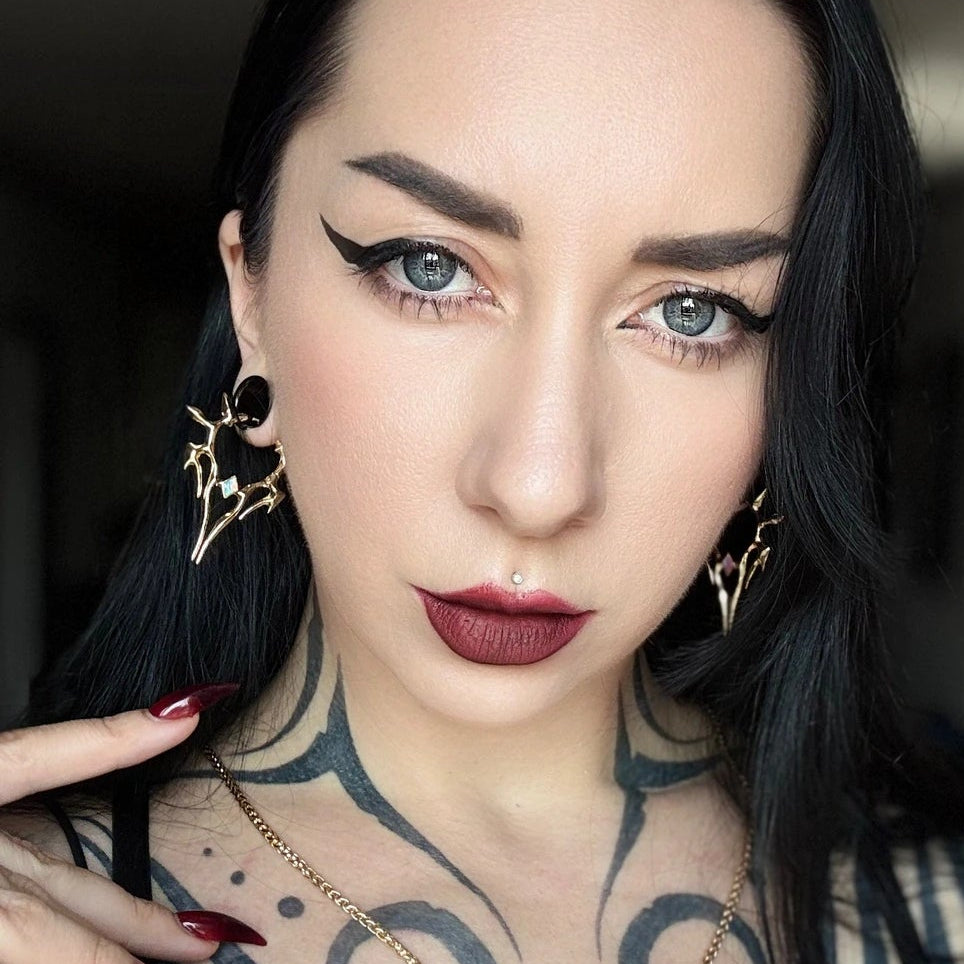 solar guardian earrings shown in a model view, featuring gold spiked geometric hoop earrings with dark center stones worn on both ears