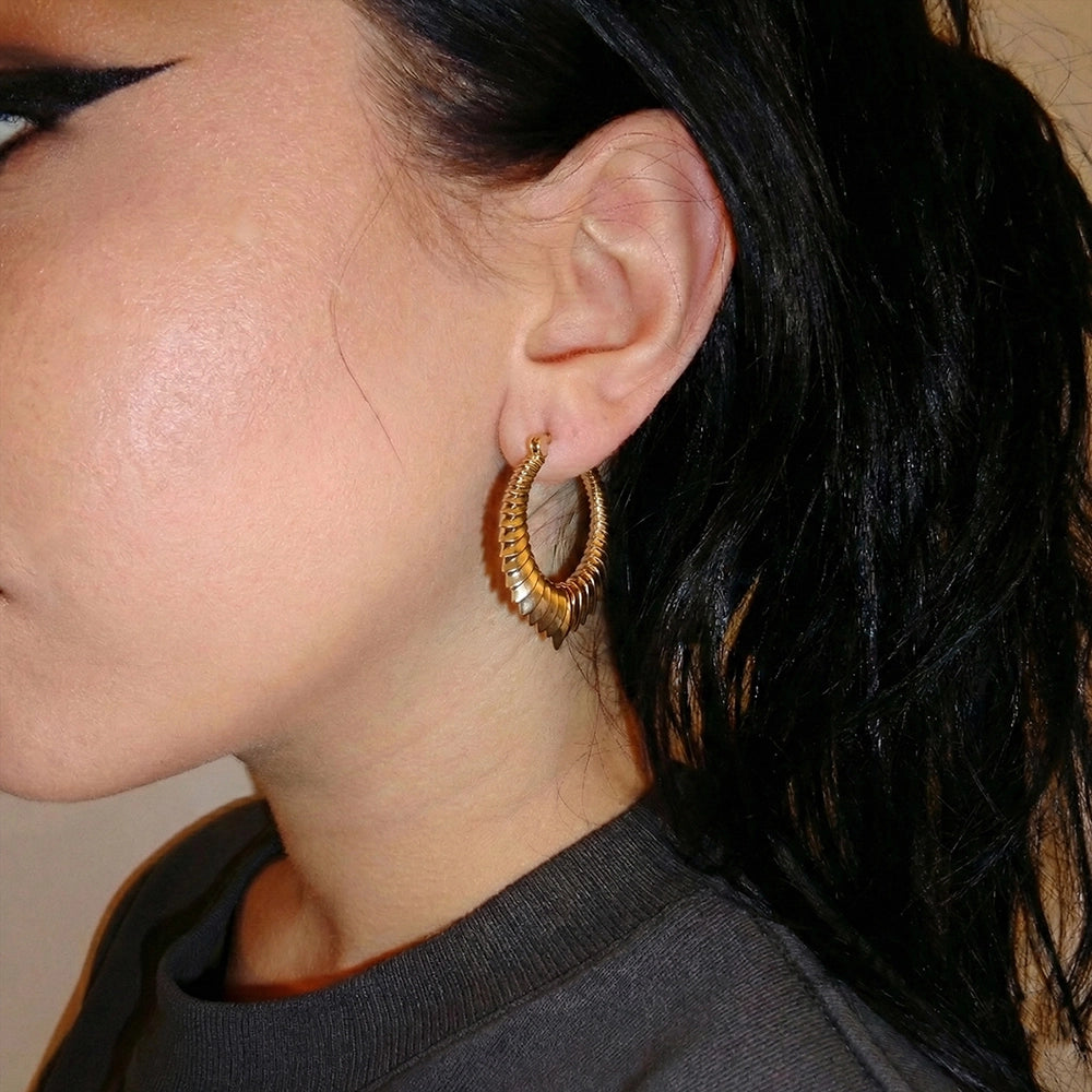 Close-up side view of a person wearing a gold-tone spine hoop earring
