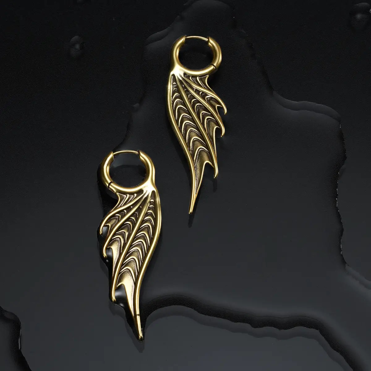 Gold Spined Wing Earrings displayed on a dark wet surface, showing the ribbed wing drops and ocean relic mood.