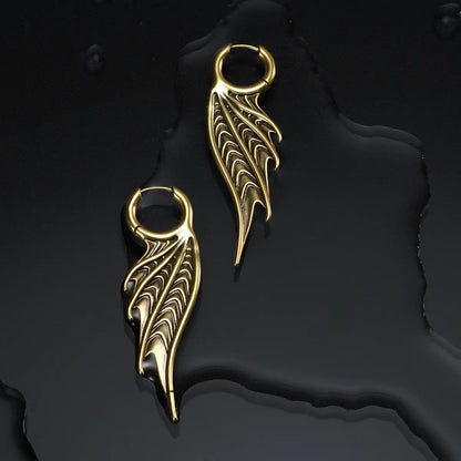Gold Spined Wing Earrings displayed on a dark wet surface, showing the ribbed wing drops and ocean relic mood.