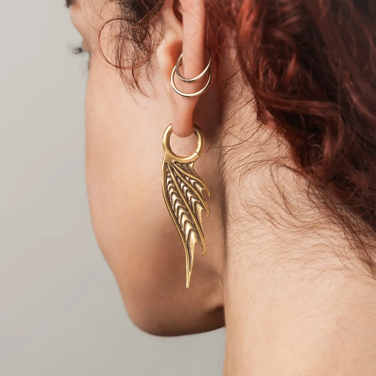 Model wearing the gold Spined Wing Earrings, highlighting the long wing-like drop shape and ribbed fin details.