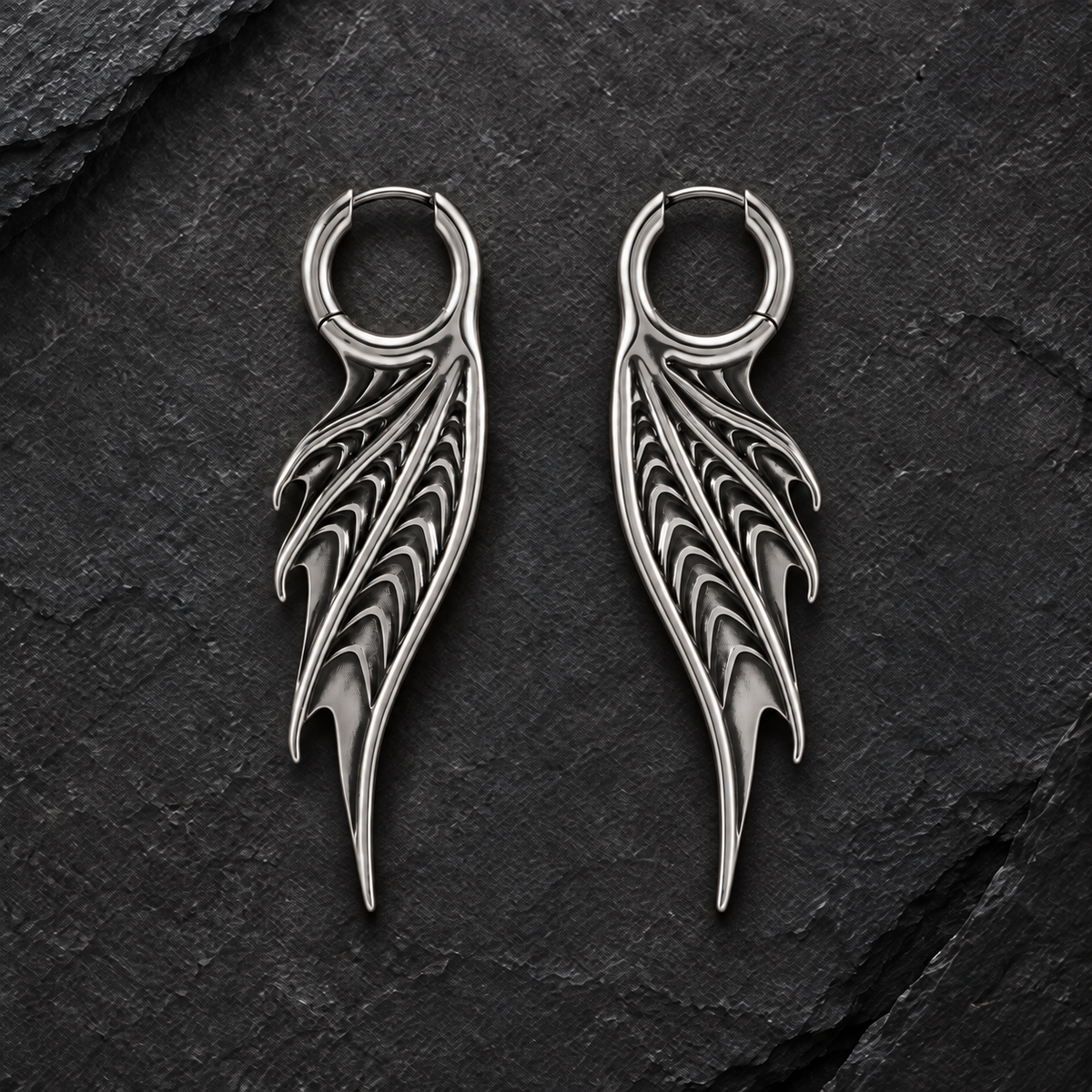 Pair of silver-tone Spined Wing hoop earrings arranged symmetrically on dark slate.