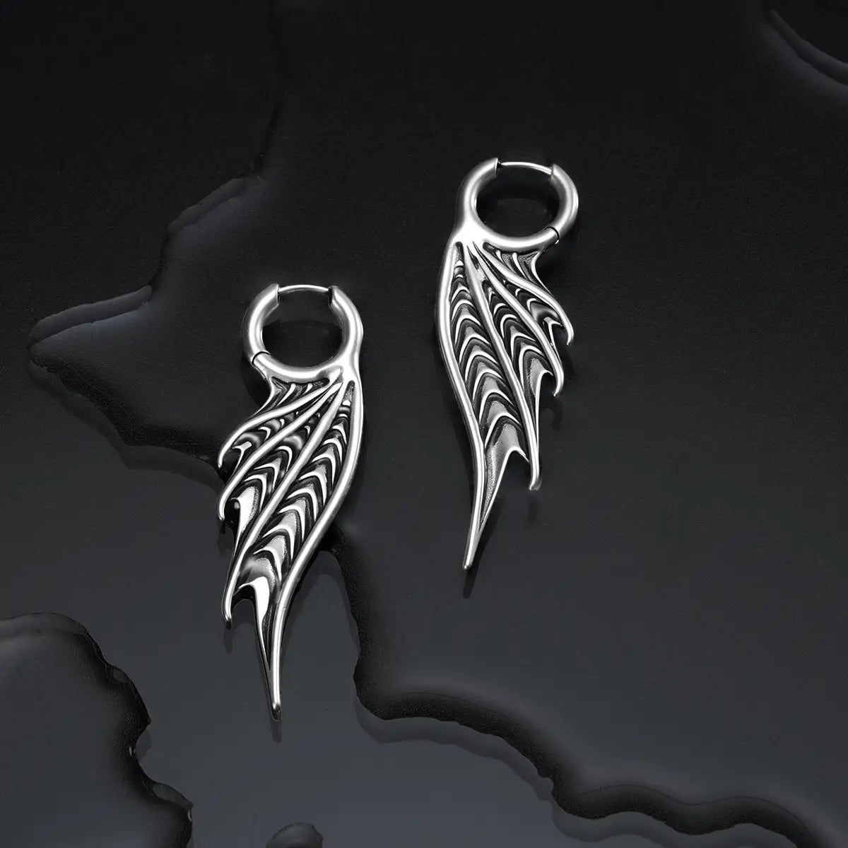 Silver Spined Wing Earrings displayed on a dark wet surface, highlighting the sharp ribbed wing shape and sea-worn gothic silhouette.